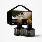 Two Het Ras car fragrance bottles with round wooden tops displayed in front of their black presentation box on a light gray background.